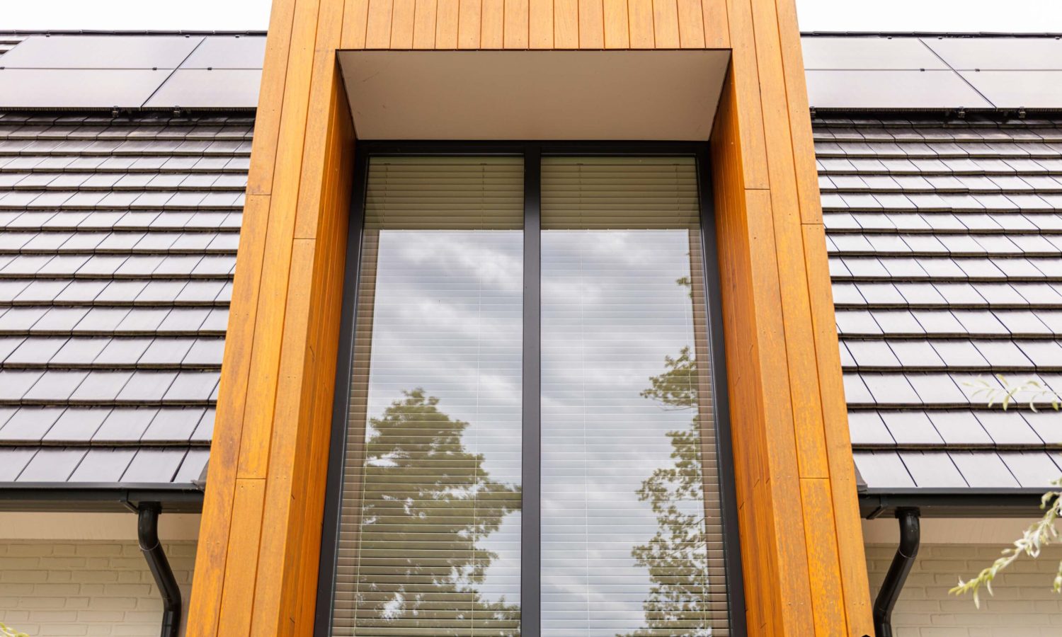 Close-up van de risaliet, uitgevoerd in siberisch larix met woodstain, omgeven door wit gesausde muren en vlakke keramische dakpannen.