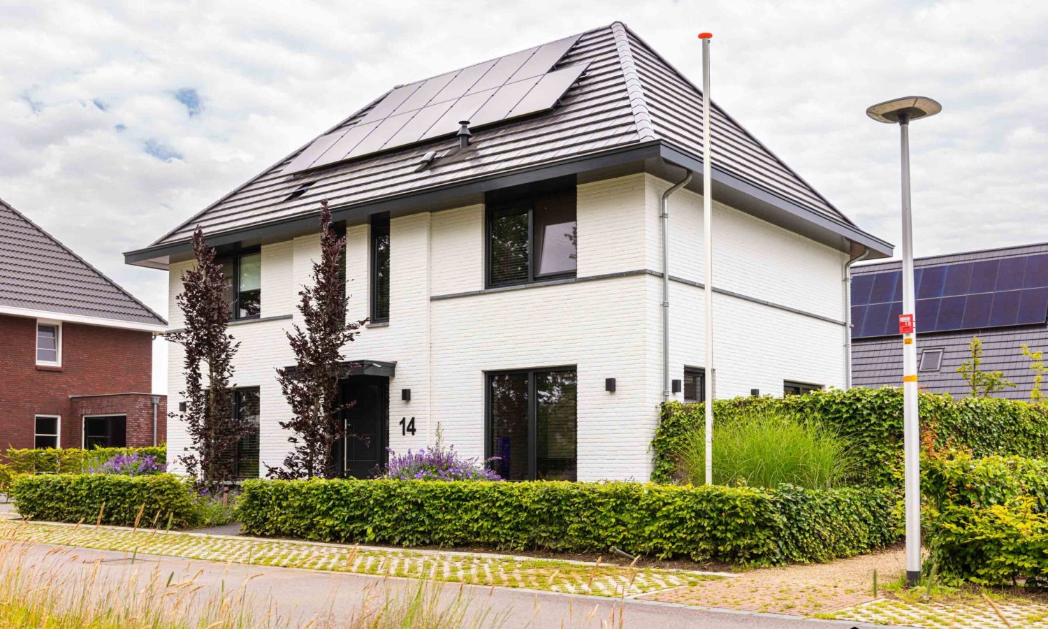 Luchtfoto van een eigentijdse notariswoning in Hengelo, uitgevoerd met wit gekeimde gevels, zwarte plint en vlakke keramische dakpannen in zwart/grijs. Voorzien van zonnepanelen en een Daikin luchtwater warmtepomp.