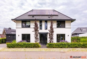 Voorzijde van een eigentijdse notariswoning met wit gesausde gevel, zwarte plint en wildverband met spekband. Strakke entree met een deur met horizontale groef en antraciet zwarte betonnen raamdorpels.