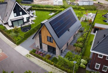 Luchtfoto van de woning en omgeving, waarop de moderne schuurwoning, zonnepanelen en het groene landschap te zien zijn