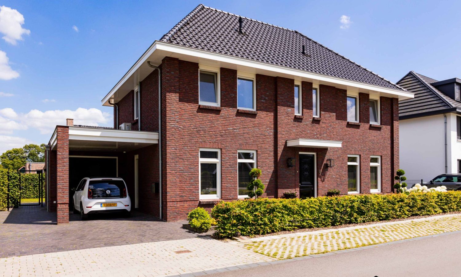 Schuin aanzicht van de woning, met een luifel boven de voordeur en een overdekte carport. De woning heeft een klassieke uitstraling met eigentijdse details.