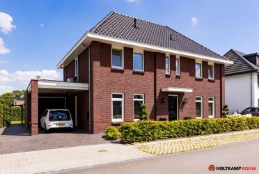 Schuin aanzicht van de woning, met een luifel boven de voordeur en een overdekte carport. De woning heeft een klassieke uitstraling met eigentijdse details.