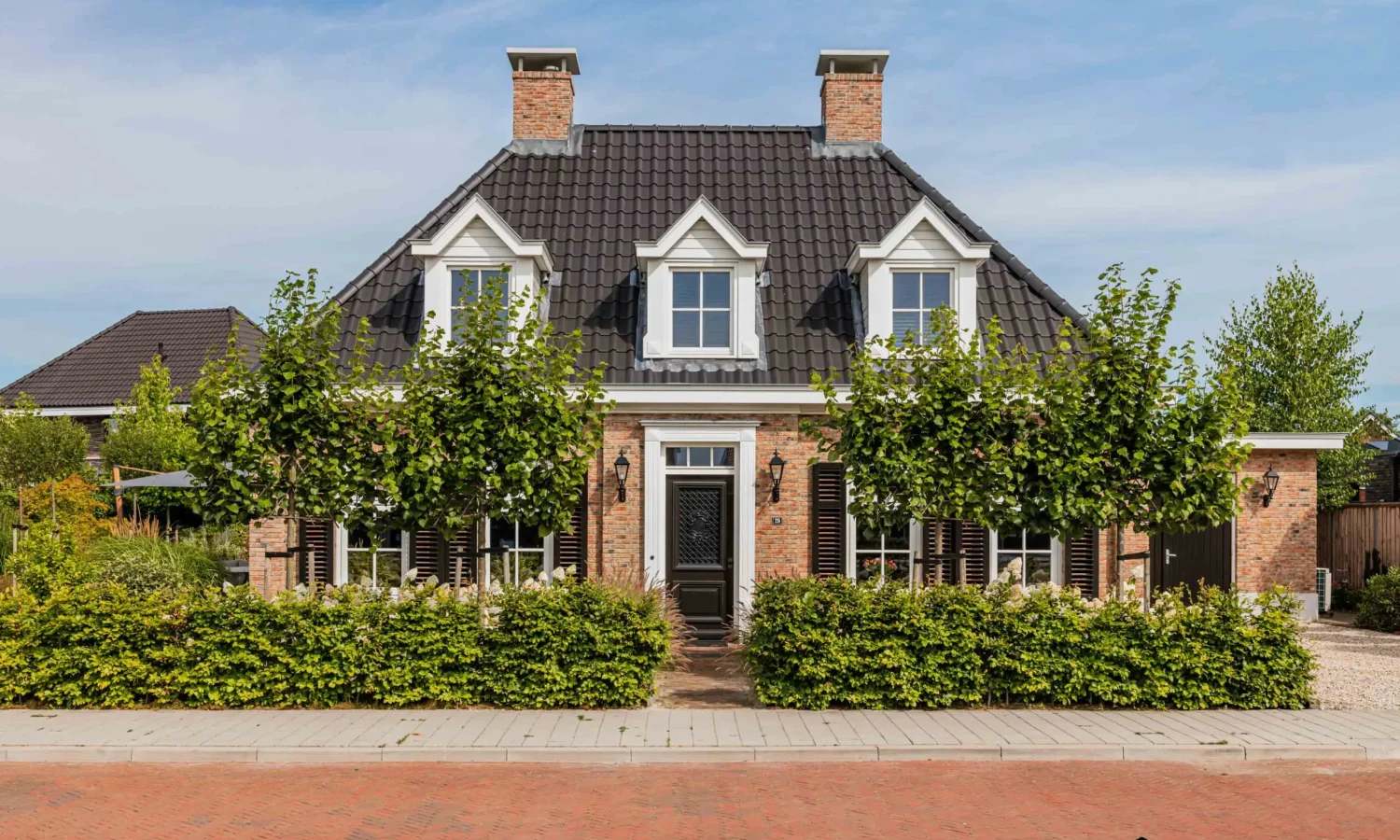 Voorzijde van een traditionele notariswoning met een eigentijds karakter, voorzien van een symmetrische gevel, twee schoorstenen en klassieke dakkapelle