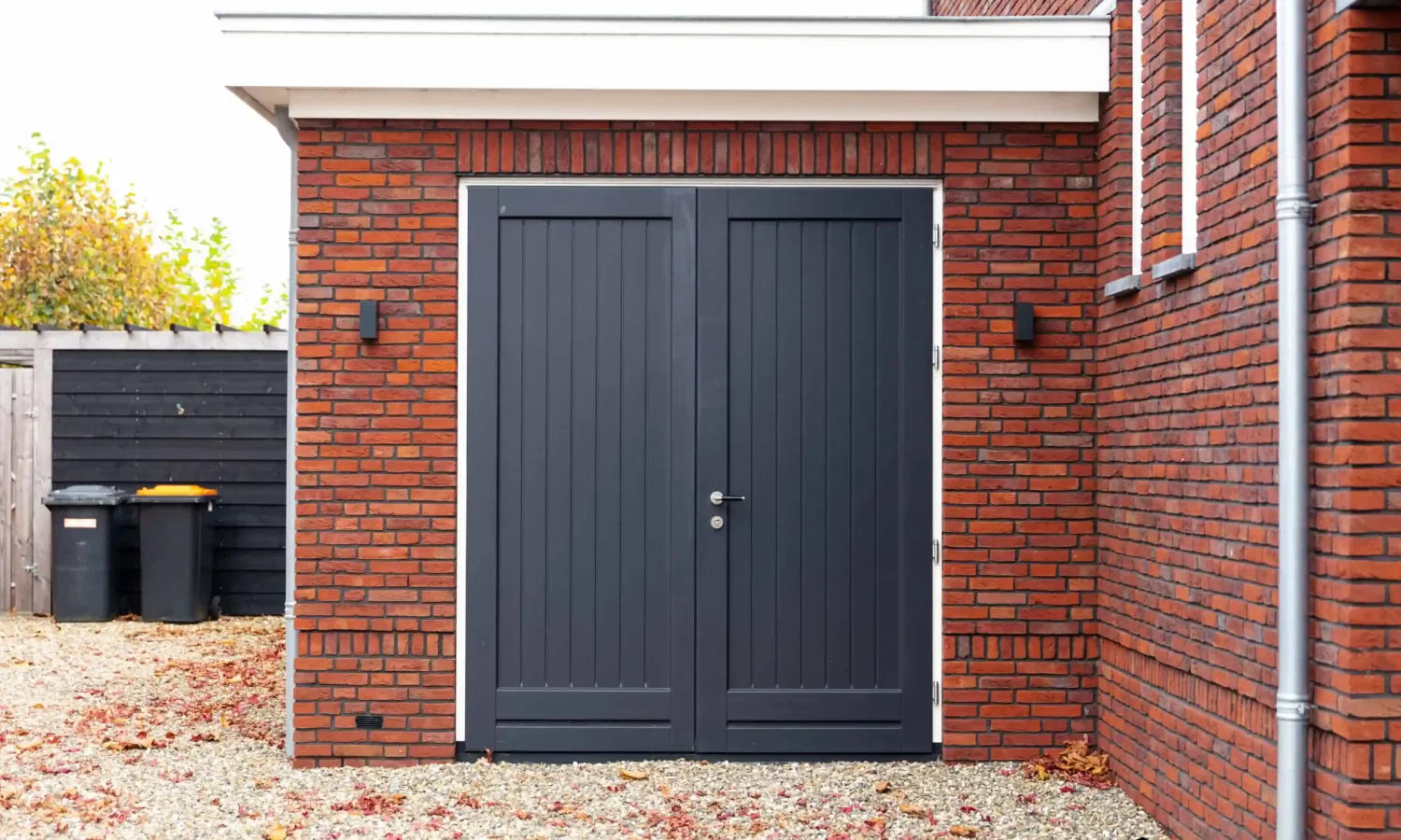 Moderne garage met dubbele deuren en bakstenen gevel, voorzien van een getimmerde bakgoot, onderdeel van een breedte gesitueerde woning in Haaksbergen – Holtkamp Bouw