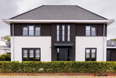 Strakke voorgevel met spekbanden en zwart-witte gevelafwerking, voorzien van een luifel boven de voordeur.