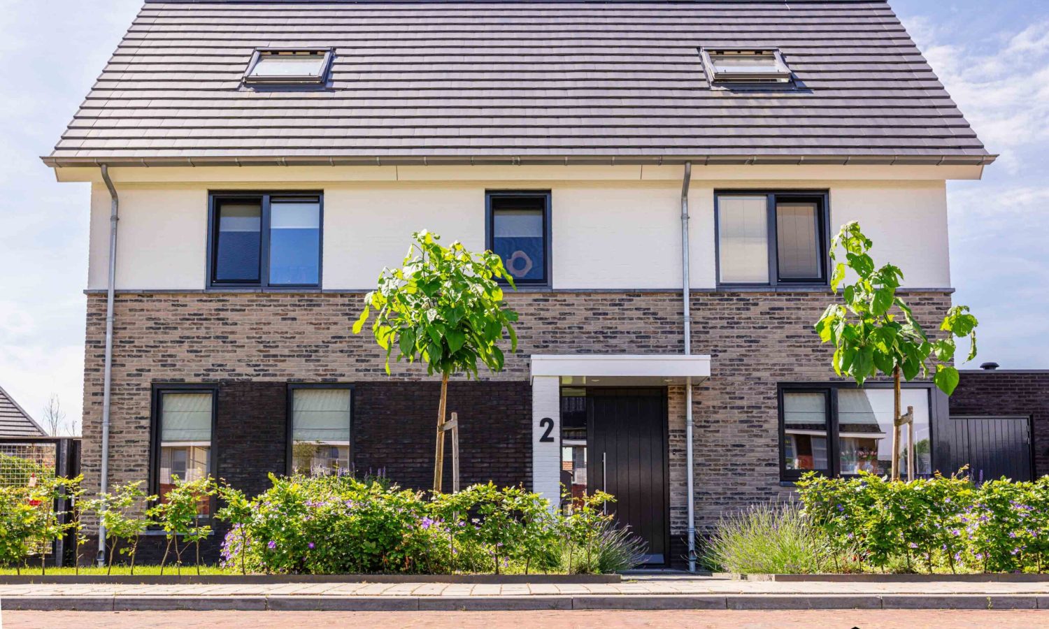 Architectonisch eigen ontwerp van Holtkamp Bouw: stijlvolle breed opgezette woning met spekband, donkere plintsteen en hoogwaardige afwerking.