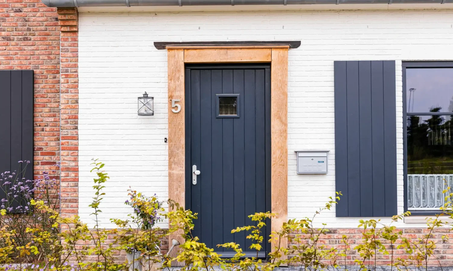 Close-up van de entree met robuuste houten omlijsting en zwarte voordeur, benadrukkend de combinatie van modern en landelijk