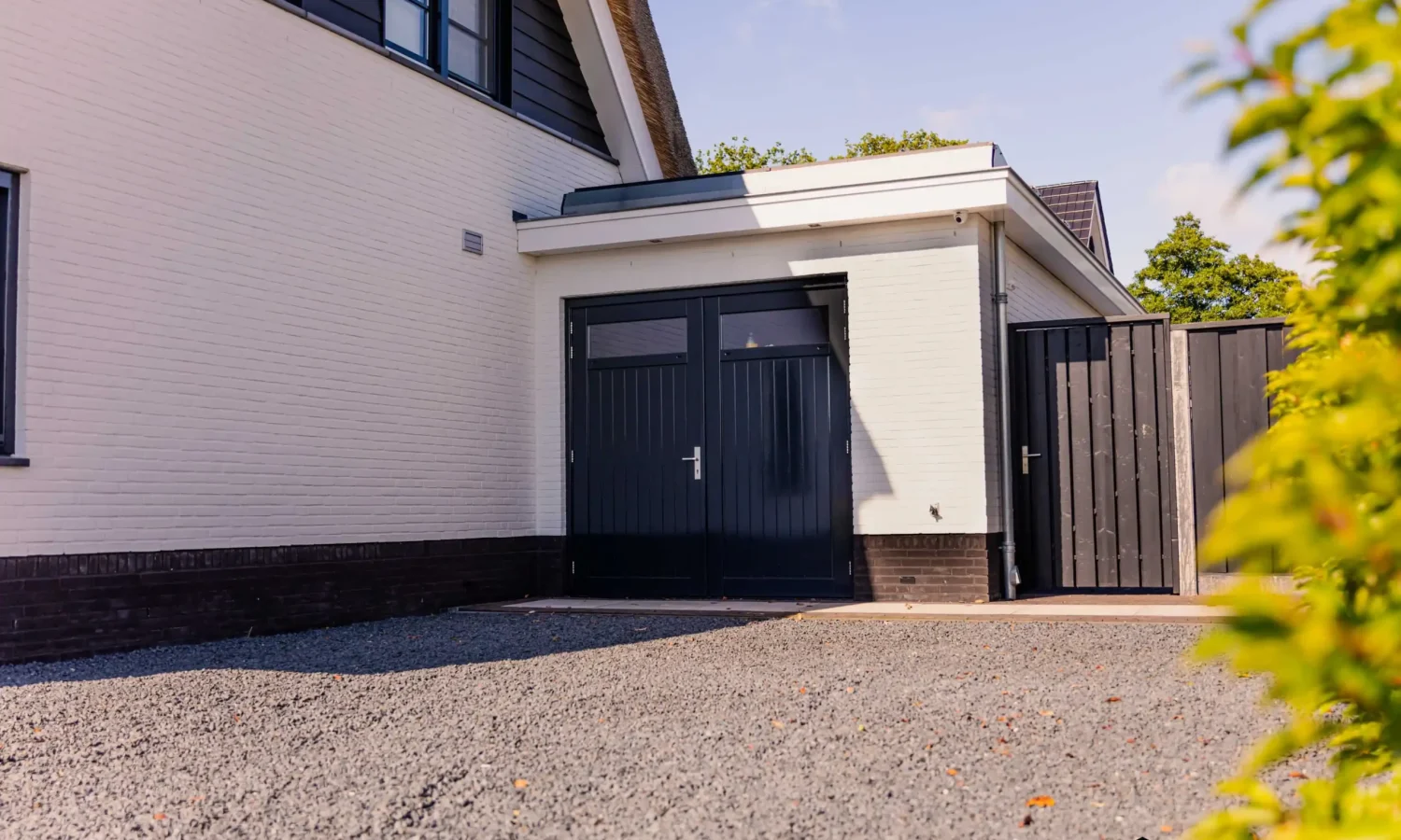 Vrijstaande berging met zwarte dubbele deuren en wit gekeimde gevel.